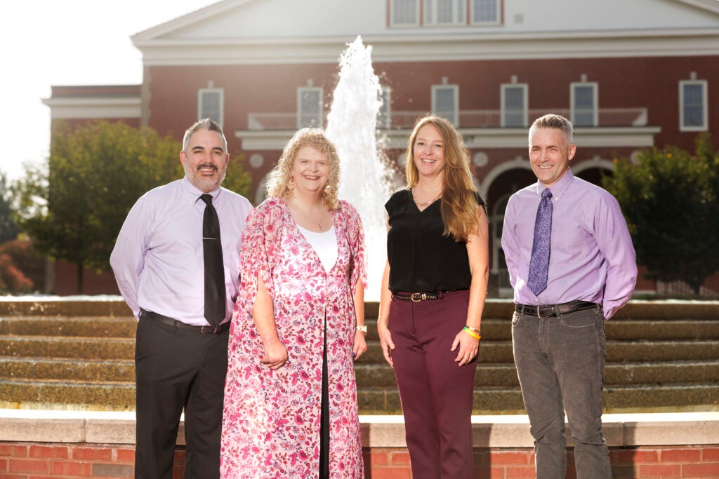 Four smiling faculty members standing in front of a fountain.